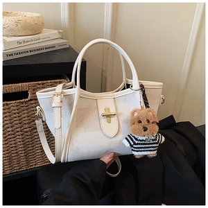 Detail of cream canvas tote with metal lock, leather trim, and cute bear charm