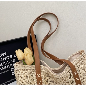 Detail of woven straw tote bag featuring brown leather straps with white cross stitching