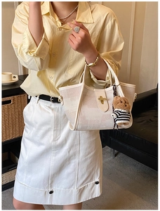 Close-up of beige woven handbag with gold twist lock and a cute plush bear charm
