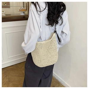 Detail of the woven texture and dark shoulder strap on the beige straw tote bag
