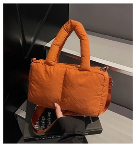 Detail of orange quilted puffer bag texture with adjustable crossbody nylon strap