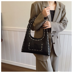 Detail of black underarm bag with silver studs and oil wax leather on a grey suit model
