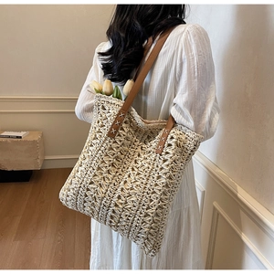 Detail of hand-woven straw tote with brown leather straps and white cross-stitch accents