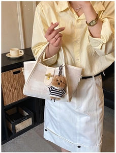 Detail of cream canvas tote bag with gold twist lock and cute teddy bear charm