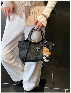 Detail of black textured tote bag featuring a gold twist lock and a cute plush dog charm