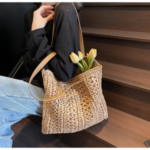 Close-up of a woven straw tote bag with brown leather shoulder straps on a wooden step