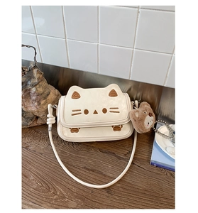 Close-up of cream cat-shaped crossbody bag with brown embroidery and bear plush charm
