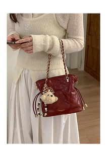 Detail of burgundy quilted chain bag with drawstring and cute bear charm on a model