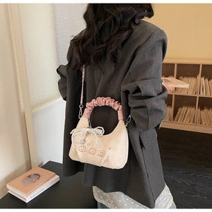 Detail of off-white crescent bag with pink pleated handle and lace bow decoration