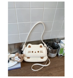 Detail of white cat-themed crossbody bag with brown embroidery and plush bear charm