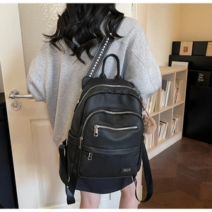 Black pebble leather backpack featuring a patterned woven strap and a plush charm detail