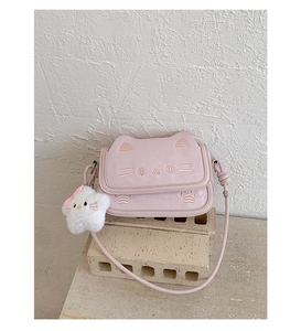 Detail of pink cat-shaped crossbody bag featuring cute embroidery and plush ball pendant