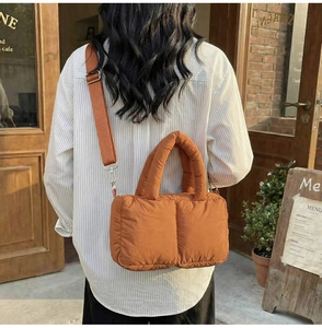 Detailed back view of orange quilted shoulder bag with wide strap in cafe setting