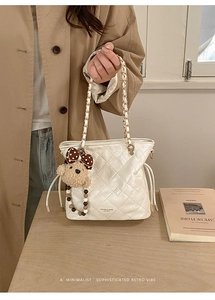 Detail of quilted off-white bucket bag with chic chain strap and plush bear charm