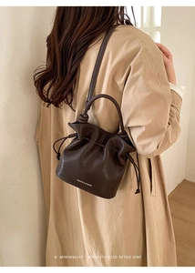 Détail du sac seau marron foncé à cordon avec logo doré sur mannequin en trench kaki