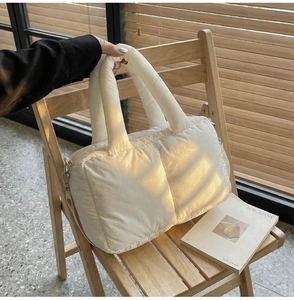 Close-up of quilted ivory puffer tote bag with padded handles on a wooden chair