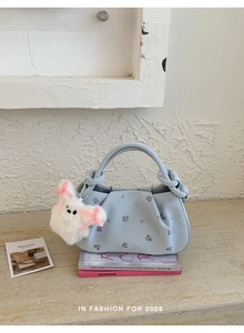 Detail of light blue dumpling bag with floral embroidery and white plush bunny charm