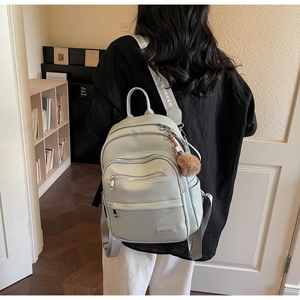 Detail of mint green faux leather backpack with multiple zipper pockets and pompom charm