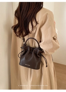 Détail du sac seau marron foncé à cordon avec texture cuir et logo de la marque