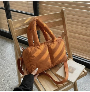 Detailed view of orange quilted puffer tote bag on a chair under sunlight shadow