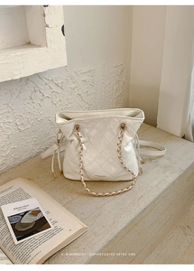 Detail of white quilted bucket bag with gold chain strap on stone stairs