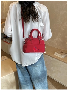 Détail du sac rouge avec broderie poney, porté avec une chemise blanche et un jean