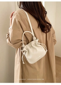 Détail du sac seau crème à cordon avec poignée nouée et lettrage de style rétro