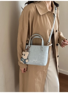 Détail du sac à main bleu clair avec breloque ours porté sur un trench-coat kaki