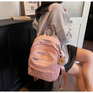 Detail of pink faux leather backpack with jacquard straps and brown pompom charm
