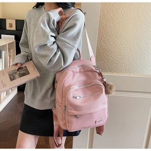 Detail of pink faux leather backpack featuring dual zippers and a brown plush pendant