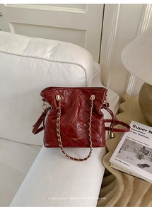 Detail of burgundy quilted leather bucket bag with gold chain strap on a white sofa