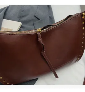 Detail of dark brown leather crescent bag with gold studs and knotted leather zipper pull