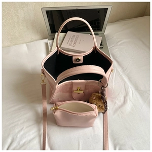 Pink bucket bag with mini pouch, gold hardware, and bear charm on a desk background