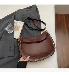 Detail of dark brown leather hobo bag featuring gold studs and adjustable strap on white bedding