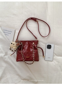Detail of burgundy quilted bucket bag with gold chain and plush bear charm