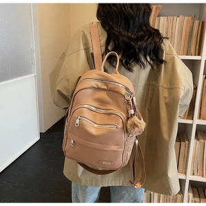 Close-up of khaki litchi grain leather backpack with three zippers and fur ball charm