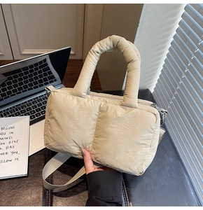 Detail of quilted beige puffer tote bag shown in casual office setting next to a laptop