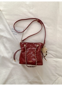 Close-up of wine red quilted bucket bag with gold chain and plush ball charm accessory