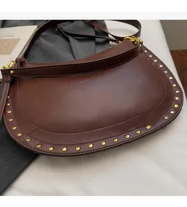 Detail of a brown half-moon saddle bag featuring gold rivets and smooth leather material
