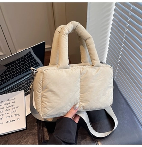 Detail of a beige quilted puffer tote bag with round handles and long textile strap