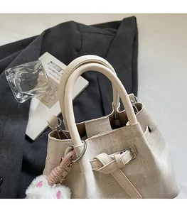 Detail der cremefarbenen Beuteltasche mit elegantem Griff und weichem Plüsch-Anhänger