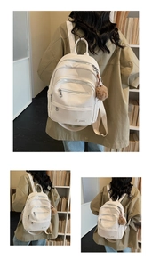 Detail of white pebbled leather backpack with multi-zipper layers and brown pompom charm