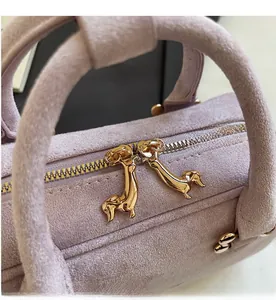 Detail of light purple suede handbag featuring unique golden dachshund-shaped double zippers
