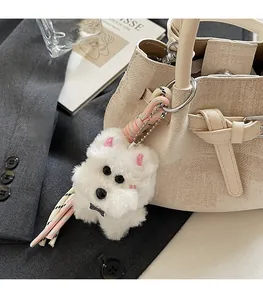 Nahaufnahme eines weißen Plüschwelpen-Anhängers an einer beigen Lederhandtasche