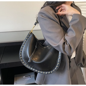 Détail d'un sac hobo en cuir noir avec rivets dorés, fermeture à pompon et bandoulière
