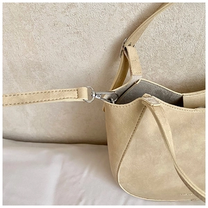 Close-up of silver metal buckle and stitching on a minimalist beige crossbody saddle bag