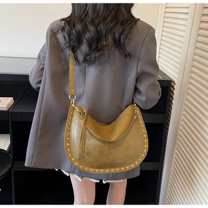 Sac hobo vert olive orné de clous dorés et de longs glands porté à l'épaule sur mannequin