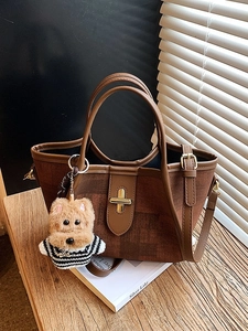 Retro brown tote bag with leather trim and teddy bear charm on a wooden surface