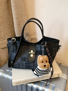 Dark grey jacquard bucket bag with gold hardware and a cute dog charm on a travel suitcase