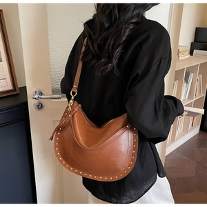 Detailed view of brown leather hobo bag with golden rivets worn by model in room